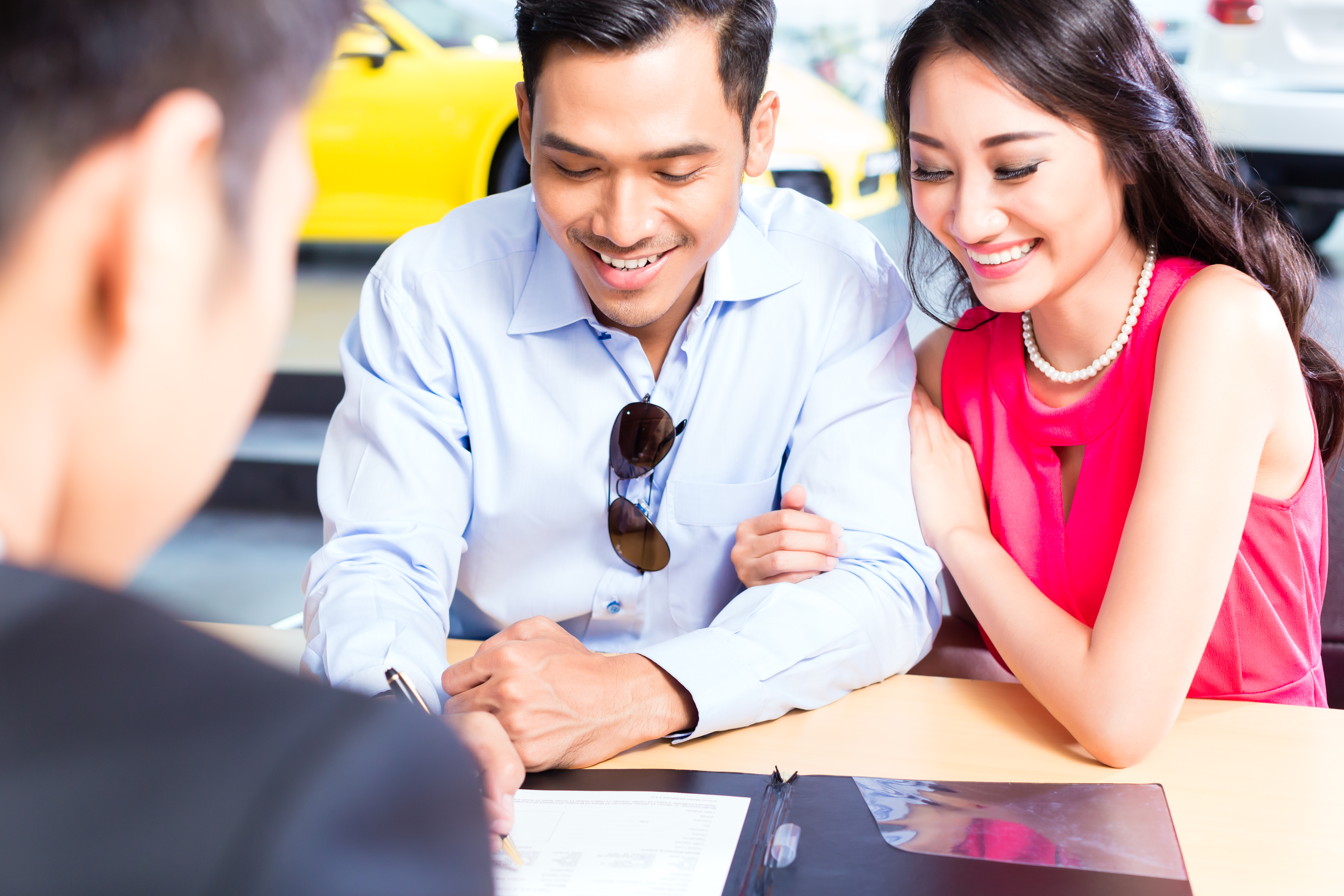 young couple signing contract in car dealership